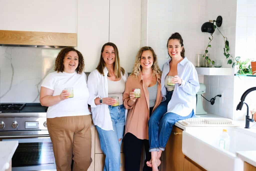 Four people pose in a kitchen while holding drinks, smiling at the camera.