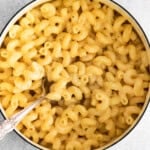 A pot of cheese pasta features tender macaroni noodles coated in creamy cheese sauce, with a silver spoon resting inside.