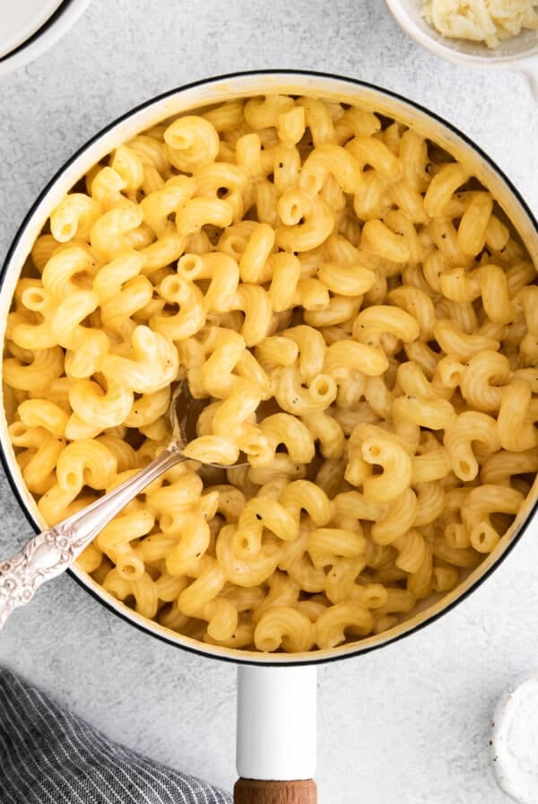 A pot filled with cooked, creamy cheese pasta with a spoon resting inside.