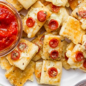 Close-up of mini cheese and pepperoni pizza bites on a plate with a small bowl of marinara dipping sauce.