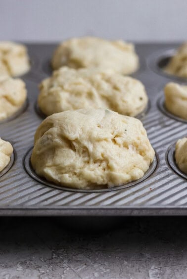 Unbaked biscuit dough portions in a metal muffin tin, ready for baking.