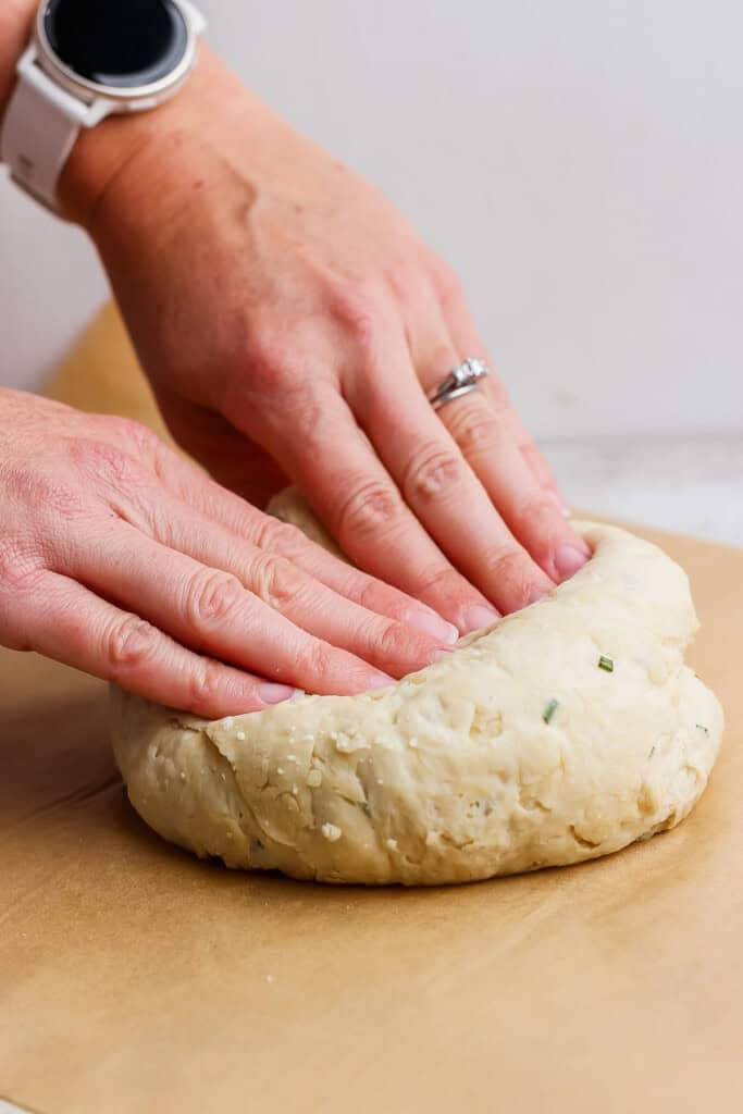 Two hands shaping a round piece of dough on a sheet of parchment paper.
