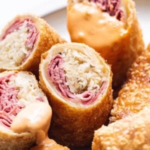 Close-up of sliced, crispy egg rolls filled with corned beef and sauerkraut, some pieces topped with a creamy orange dipping sauce.