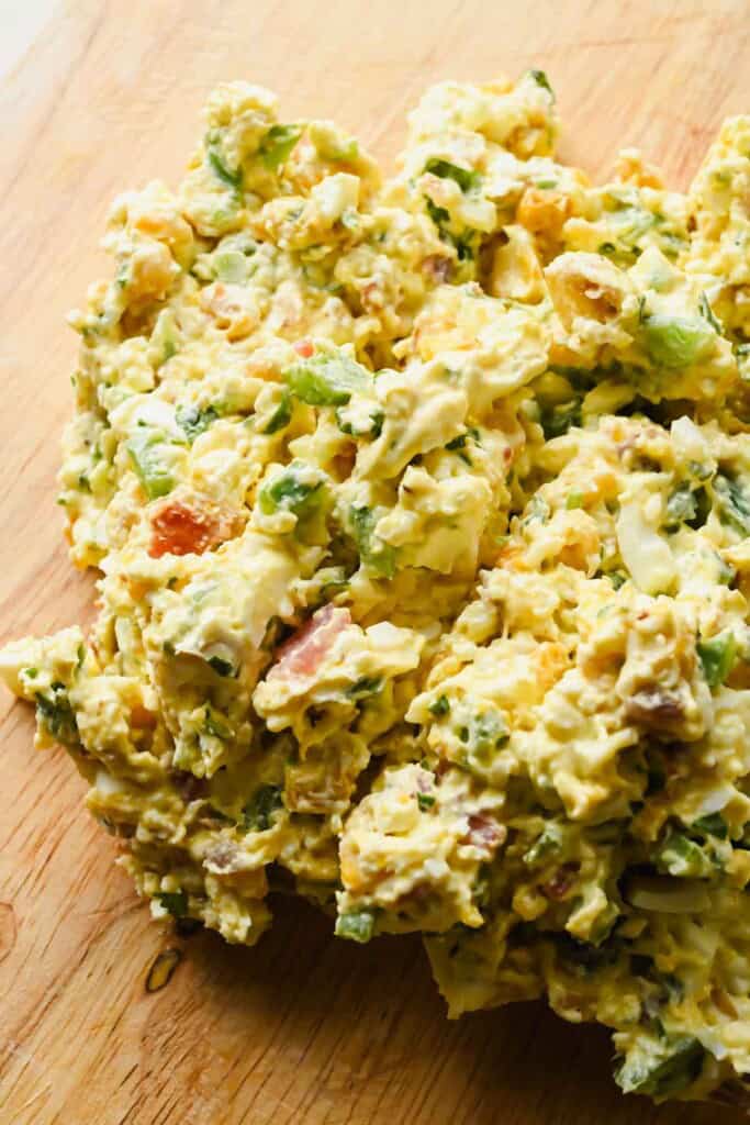 A close-up of egg salad with chopped eggs, celery, herbs, and creamy dressing on a wooden surface.