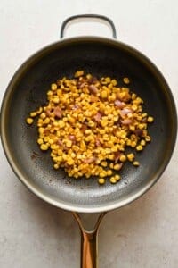 Corn and diced red onions sautéing in a non-stick skillet on a light-colored surface.