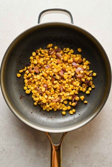Corn and diced red onions saut&eacute;ing in a non-stick skillet on a light-colored surface.