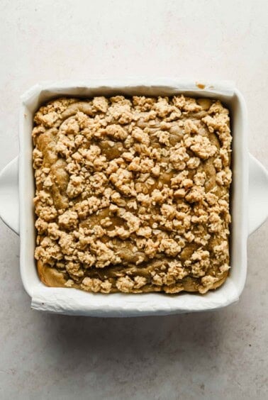 A square baking dish filled with baked crumb-topped coffee cake, photographed from above on a light surface.