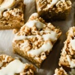 Close-up of square banana oat bars topped with a white icing drizzle, arranged on parchment paper.