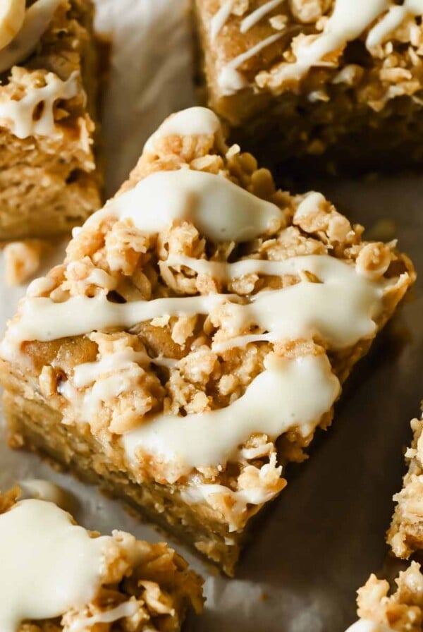 Close-up of square banana oat bars topped with a white icing drizzle, arranged on parchment paper.