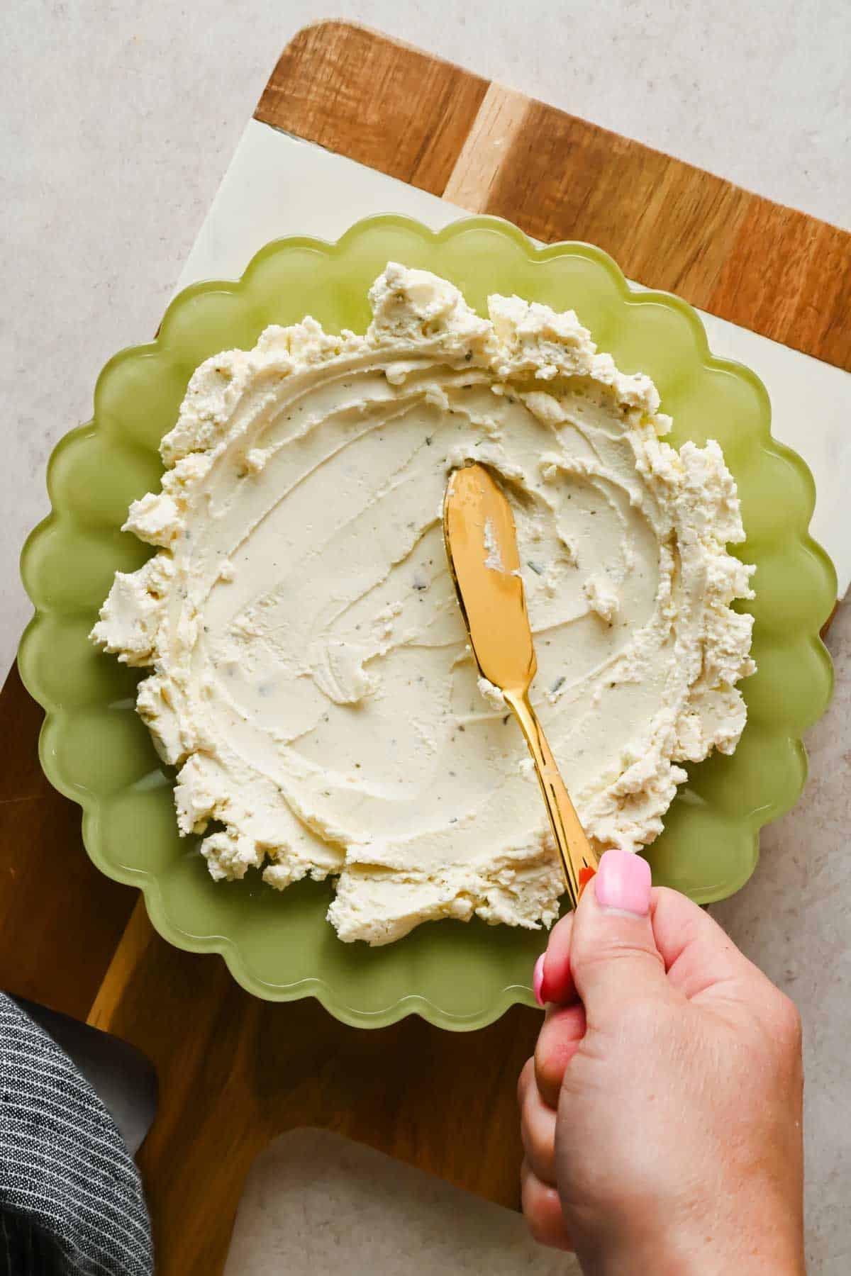 Spreading Boursin cheese into a green scalloped bowl with a gold knife