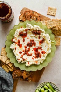 Boursin chili crunch dip on a board with crackers, toast, cucumber slices, and a jar of chili crunch