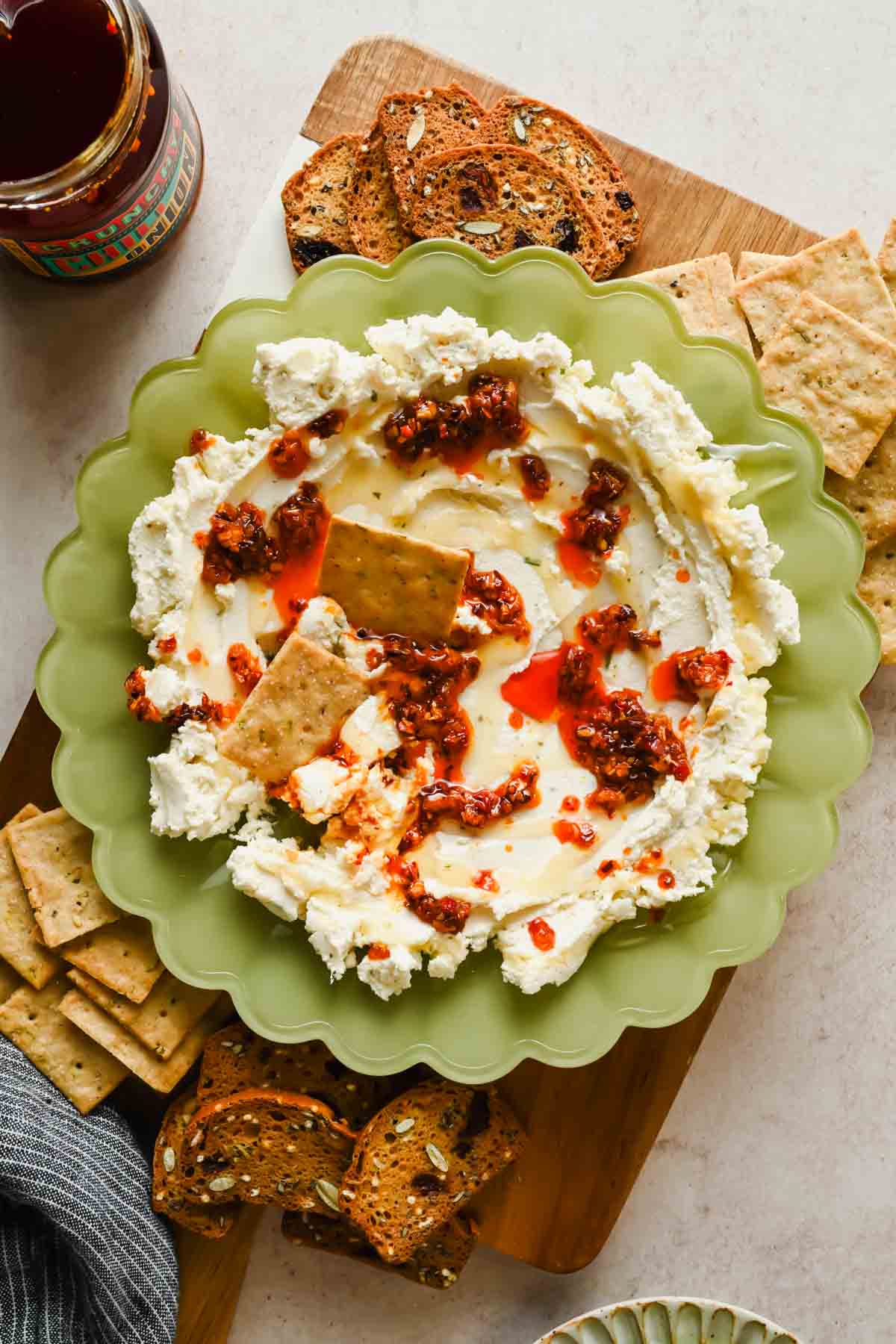 Overhead view of boursin chili crunch dip topped with chili oil and honey, served with crackers on a wooden board