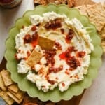 Boursin chili crunch dip in a green scalloped bowl topped with chili crunch and honey, served with crackers