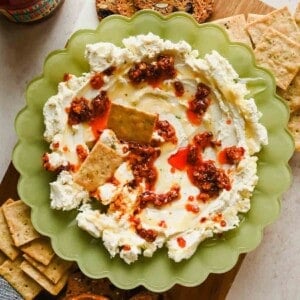 Boursin chili crunch dip in a green scalloped bowl topped with chili crunch and honey, served with crackers