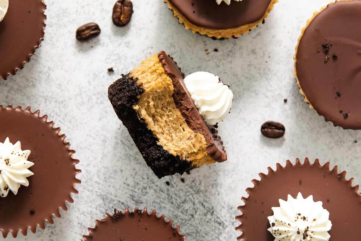 Overhead view of espresso cheesecake cups with one cut in half showing the Oreo crust, espresso filling, and chocolate ganache layers.