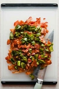 Chopped crispy bacon and roasted jalapeños on a white cutting board