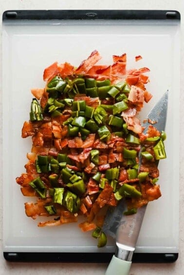 Chopped crispy bacon and roasted jalape&ntilde;os on a white cutting board