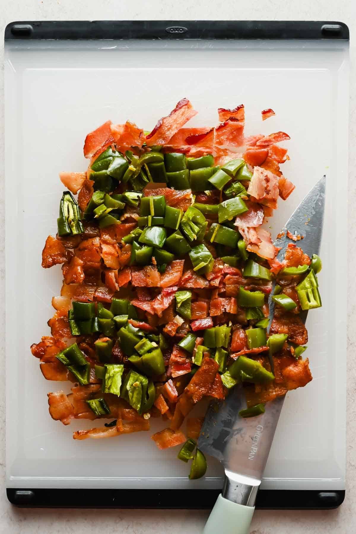 Chopped crispy bacon and roasted jalape&ntilde;os on a white cutting board