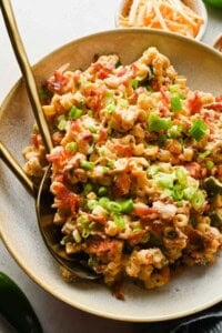 Jalapeño popper pasta salad with crispy bacon, green onions, and cheddar cheese served with gold utensils