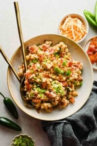Jalapeño popper pasta salad in a large bowl with crispy bacon, green onions, and shredded cheese, with gold utensils and fresh jalapeños nearby