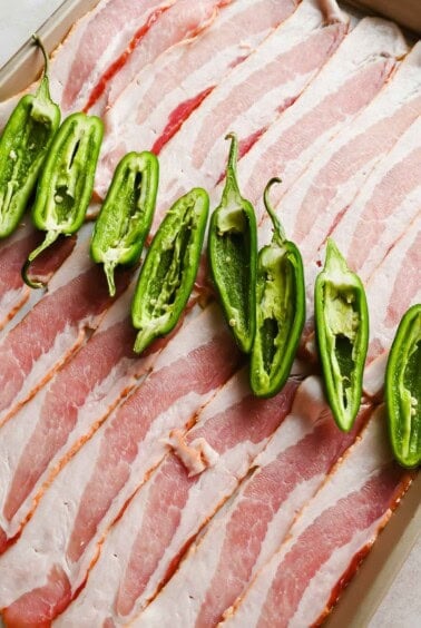 Sliced bacon and halved jalape&ntilde;o peppers on a tray before roasting