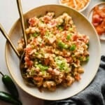 Jalapeño popper pasta salad topped with green onions and bacon in a bowl with serving utensils