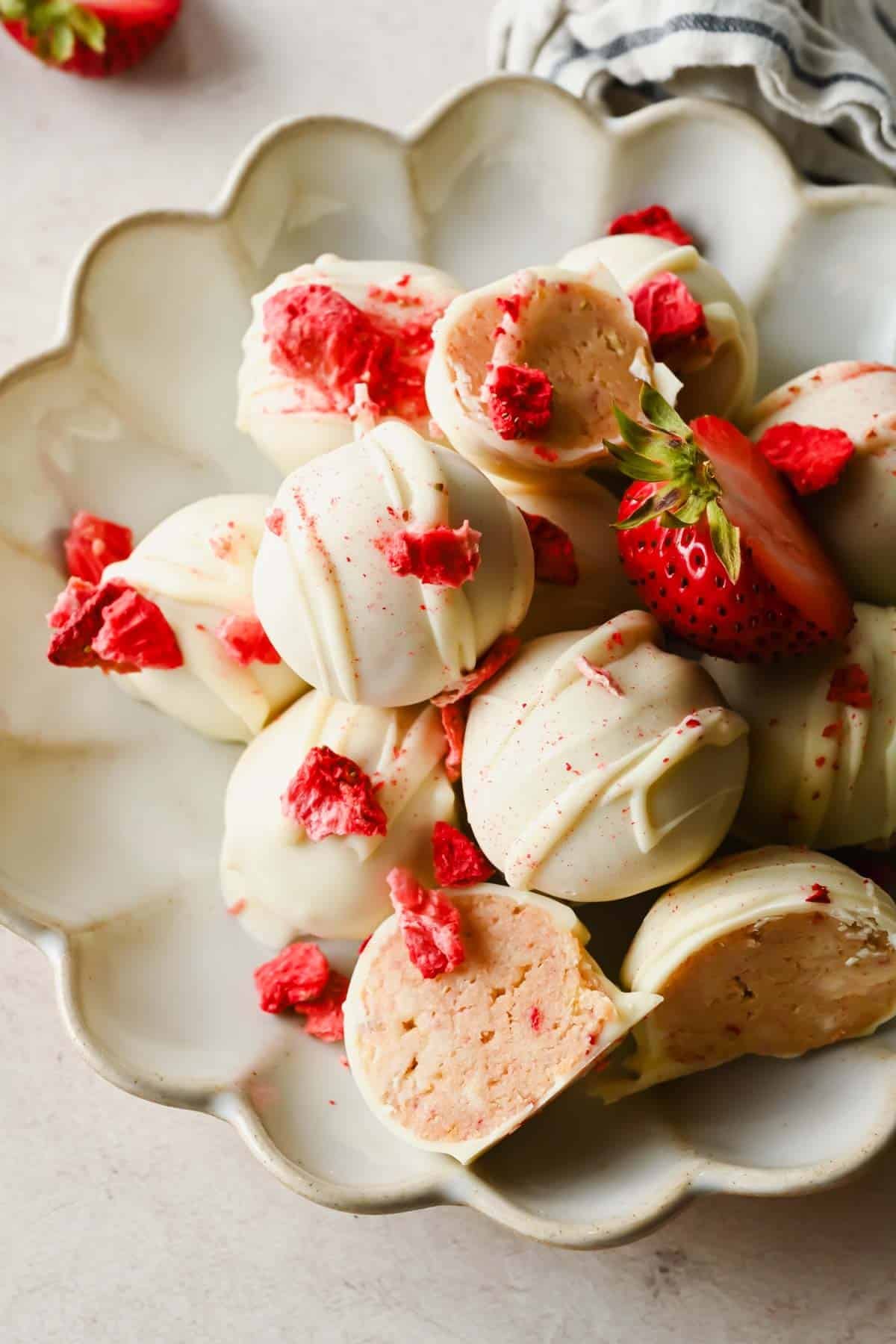 A plate of white chocolate truffles with pink strawberry pieces, some whole and some cut open to show the pink filling inside.