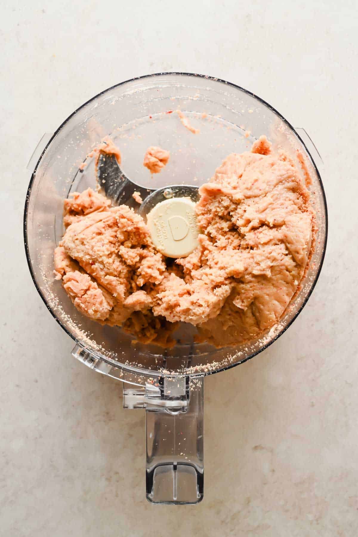A food processor containing a blended, pale pink mixture on a light countertop.
