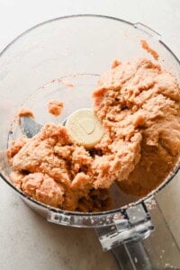 A food processor containing a ball of mixed pinkish dough, with some dough clinging to the blades and sides.