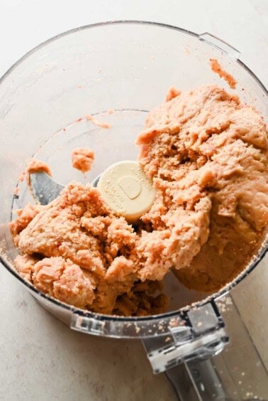 A food processor containing a ball of mixed pinkish dough, with some dough clinging to the blades and sides.