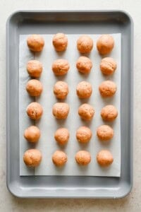 Twenty raw dough balls evenly spaced on a parchment-lined baking sheet, arranged in four rows of five.