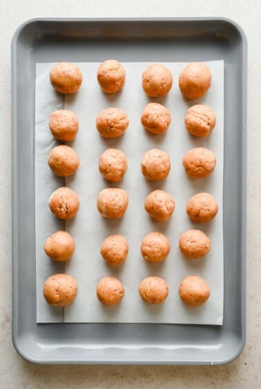Twenty raw dough balls evenly spaced on a parchment-lined baking sheet, arranged in four rows of five.