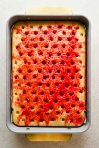 Vanilla cake with holes filled with red strawberry Jello in a baking pan
