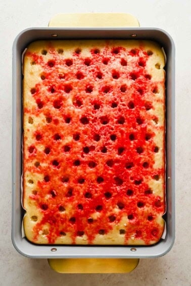 Vanilla cake with holes filled with red strawberry Jello in a baking pan