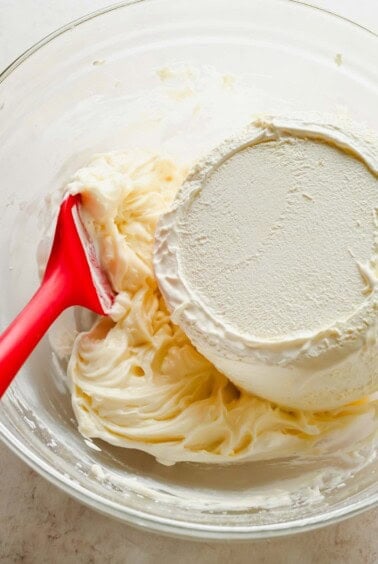 Cream cheese and powdered sugar in a glass mixing bowl for poke cake frosting
