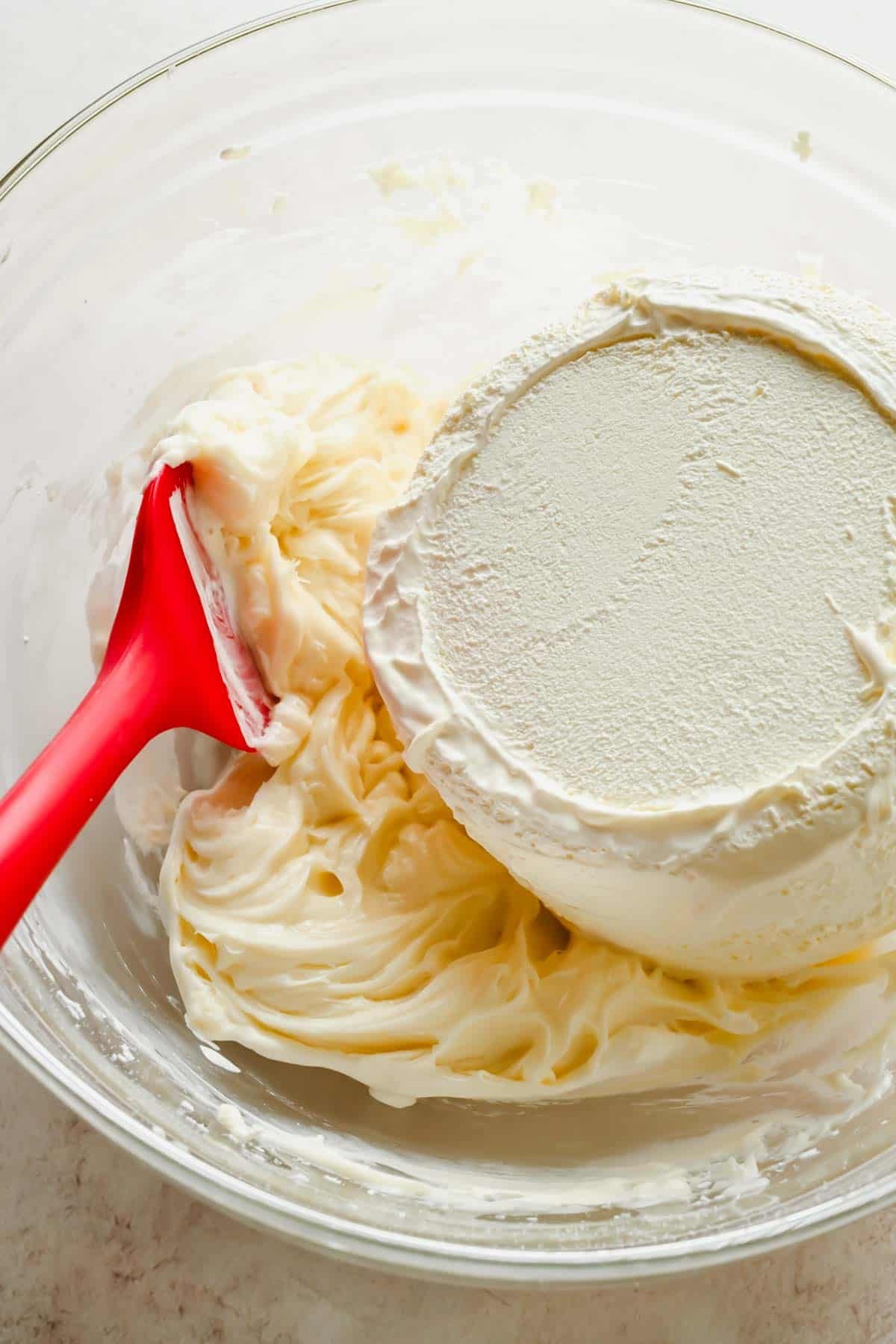 Cream cheese and powdered sugar in a glass mixing bowl for poke cake frosting