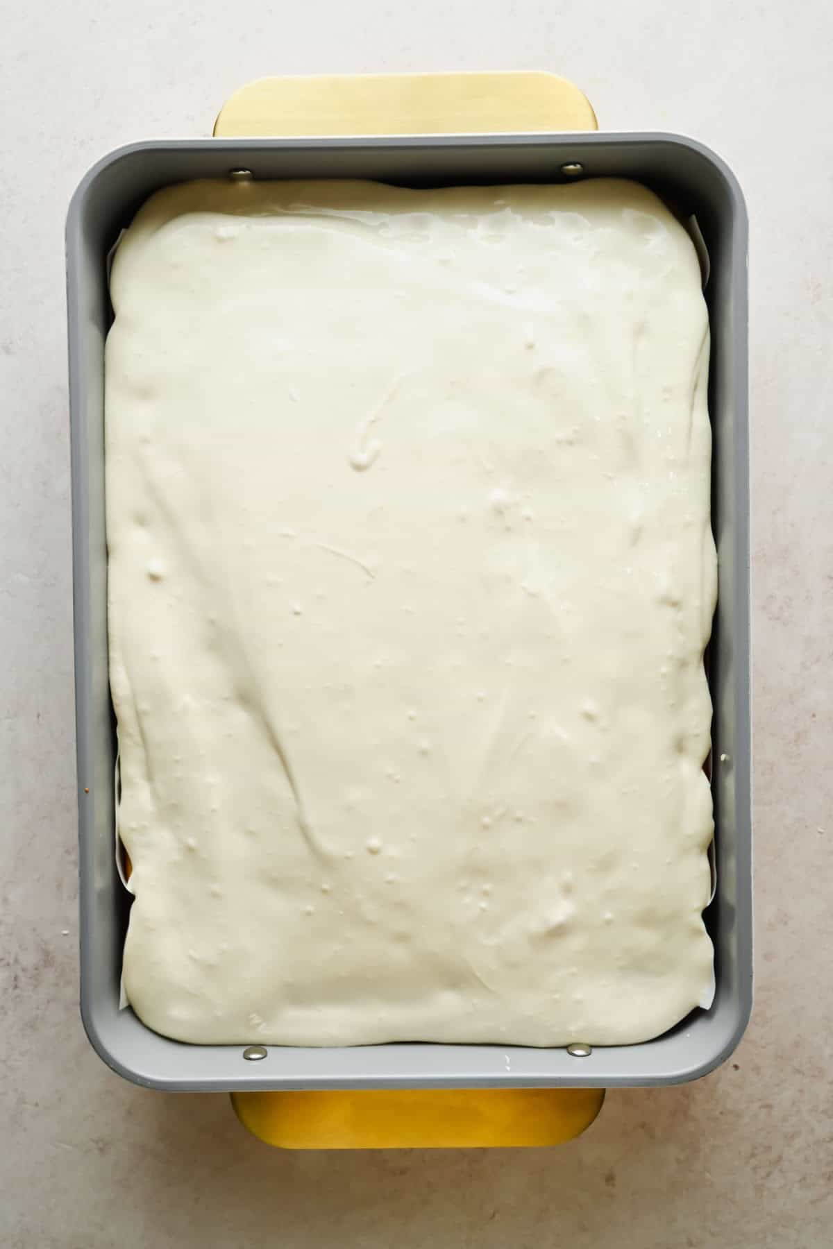 Cream cheese frosting spread over a strawberry Jello poke cake in a baking pan