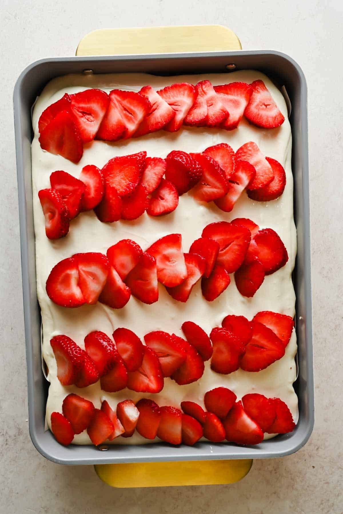 Rows of sliced fresh strawberries arranged on top of frosted poke cake