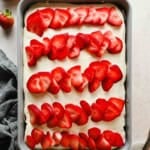 Strawberry poke cake topped with cream cheese frosting and rows of fresh sliced strawberries in a 9x13 baking pan