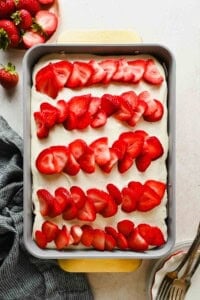 Strawberry poke cake topped with cream cheese frosting and rows of fresh sliced strawberries in a 9x13 baking pan