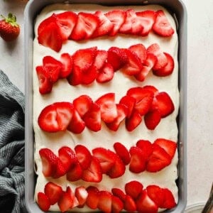 Strawberry poke cake topped with cream cheese frosting and rows of fresh sliced strawberries in a 9x13 baking pan