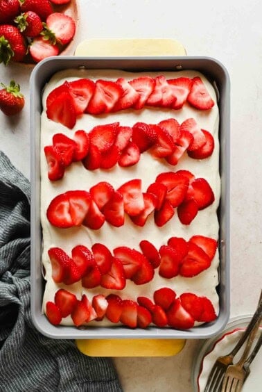Strawberry poke cake topped with cream cheese frosting and rows of fresh sliced strawberries in a 9x13 baking pan