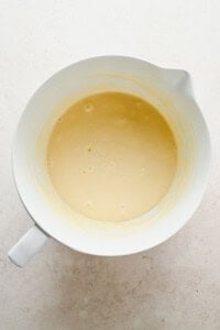 A white mixing bowl containing a smooth, light yellow batter on a pale countertop.
