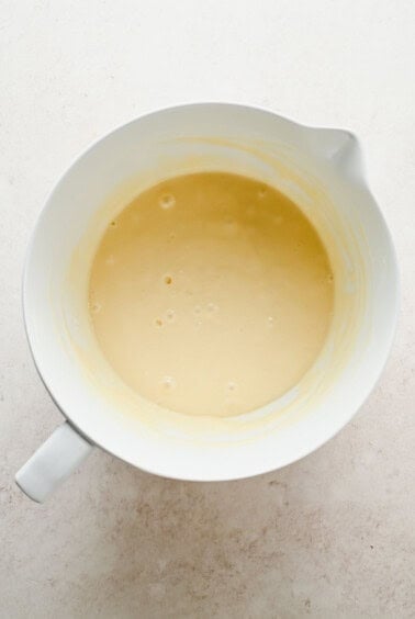 A white mixing bowl containing a smooth, light yellow batter on a pale countertop.
