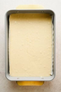 A rectangular baking pan filled with raw cake batter, lined with parchment paper, viewed from above.