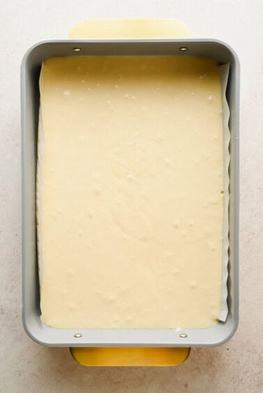 A rectangular baking pan filled with raw cake batter, lined with parchment paper, viewed from above.