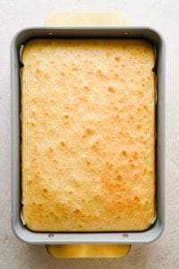 A rectangular baking pan filled with a freshly baked, golden-brown cake with a slightly uneven surface.