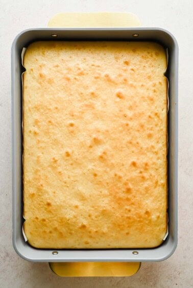 A rectangular baking pan filled with a freshly baked, golden-brown cake with a slightly uneven surface.
