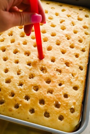 Using a straw to poke evenly spaced holes into a baked vanilla cake