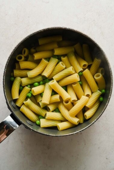 Cooked rigatoni and green peas in a pot